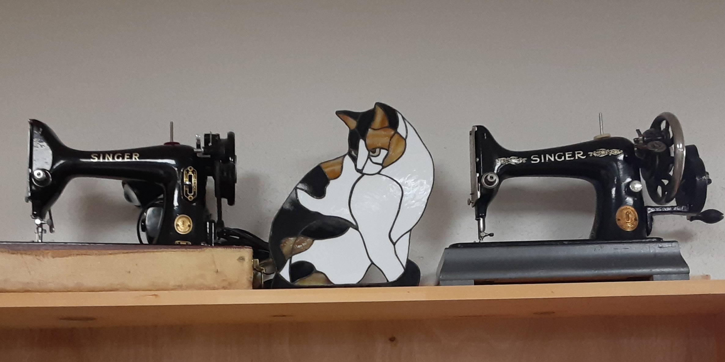 An image of a stained glass calico cat between two old sewing machines